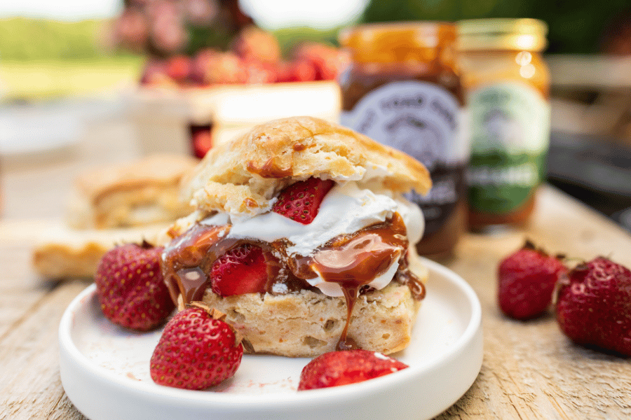 Biscuit with strawberries, cream and caramel on a plate with jars of caramel in the background.
