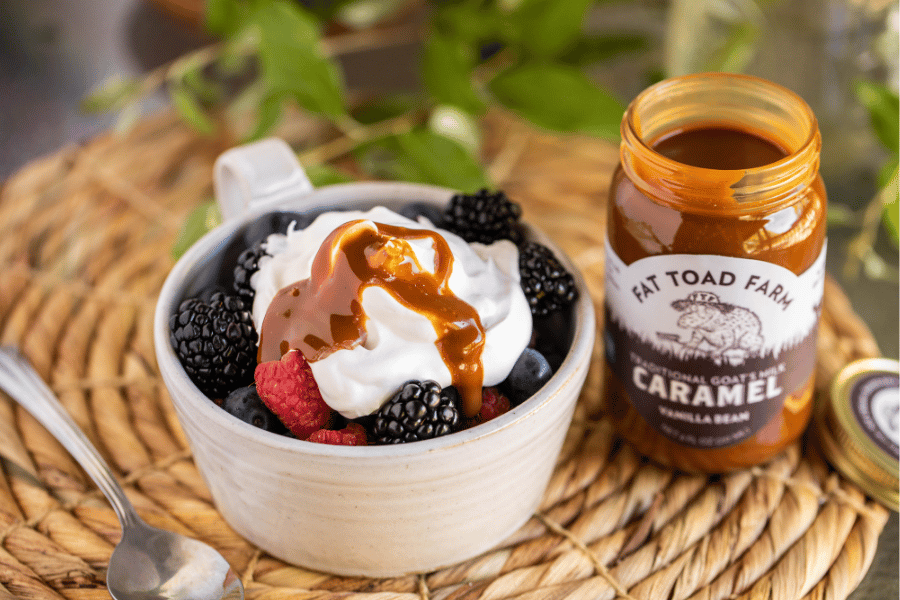 Bowl of berries with whipped cream and caramel sauce next to a jar of Fat Toad Farm caramel.