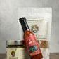 Three BBVT/Guster products including hot sauce, mustard and granola on a wooden surface with a gray background, with the hot sauce bottle leaning to the left