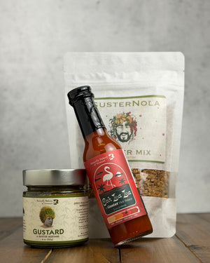 Three BBVT/Guster products including hot sauce, mustard and granola on a wooden surface with a gray background, with the hot sauce bottle leaning to the left