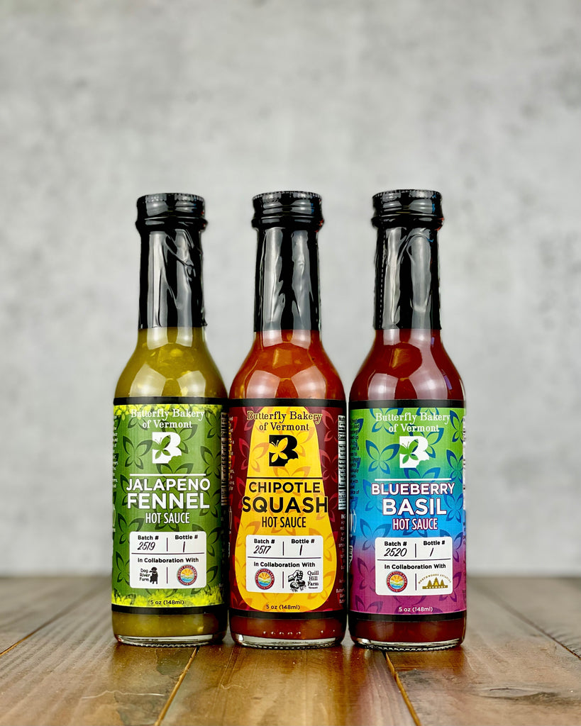 Three hot sauce bottles with colorful labels on a wooden surface.