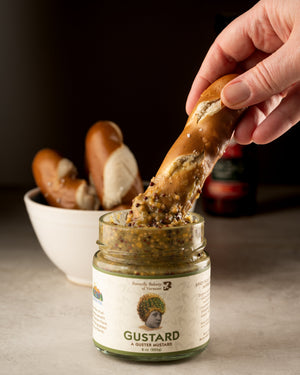 Soft pretzel stick being dipped into a jar of Butterfly Bakery of Vermont Gustard mustard
