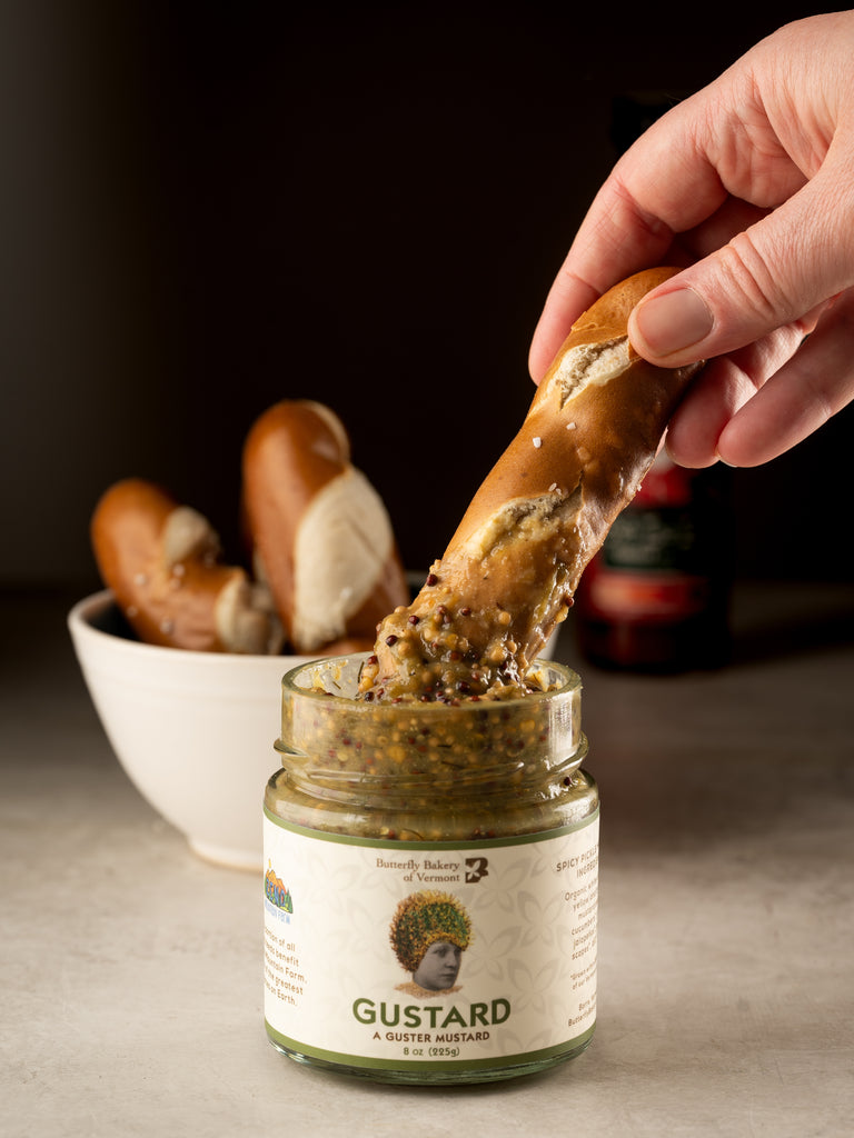 Soft pretzel stick being dipped into a jar of Butterfly Bakery of Vermont Gustard mustard