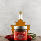 Butterfly Bakery of Vermont Maple Sriracha Mustard on a wood surface with red peppers and a bottle of maple syrup