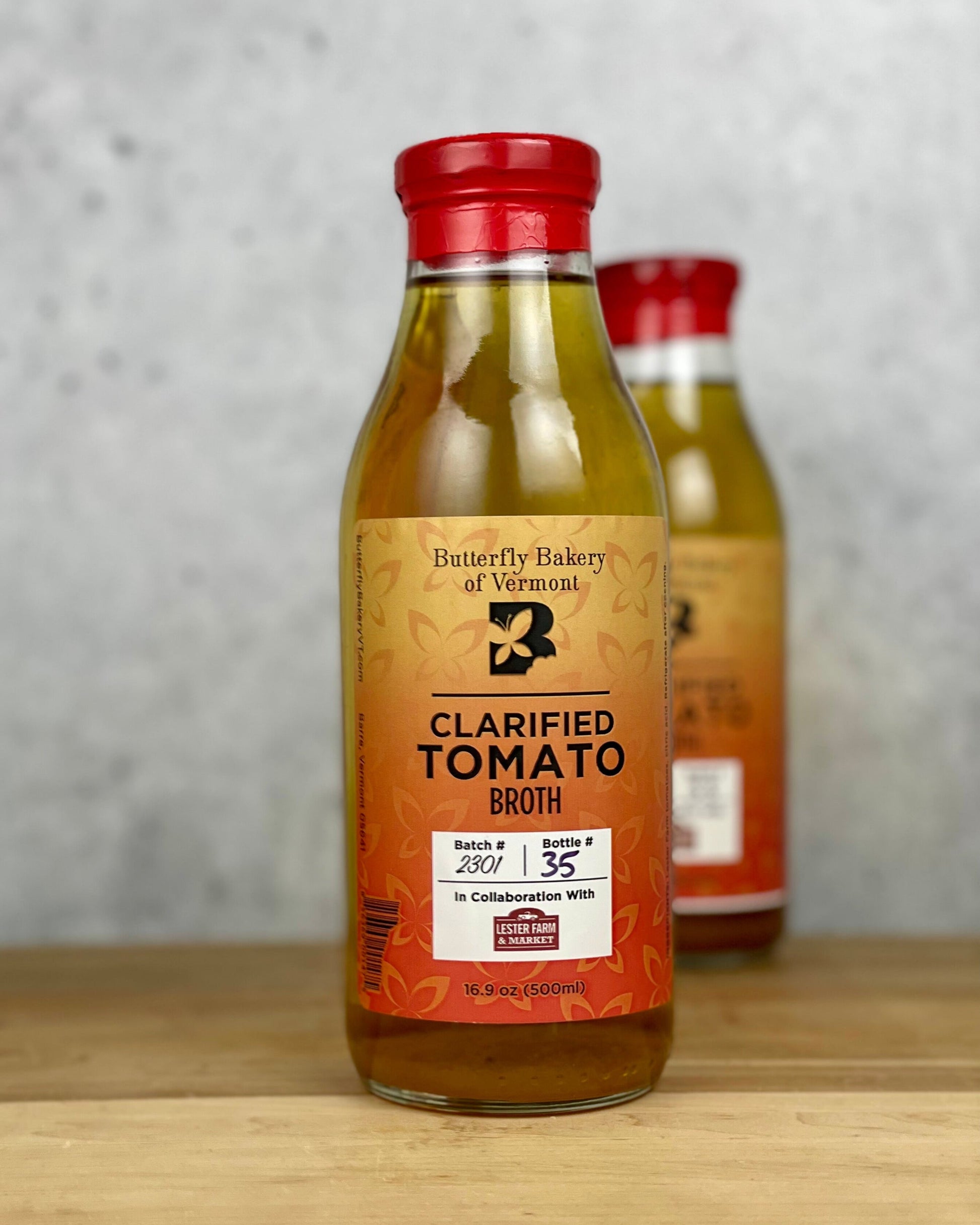 Two bottles of Butterfly Bakery of Vermont Clarified Tomato Broth sitting on a wood surface