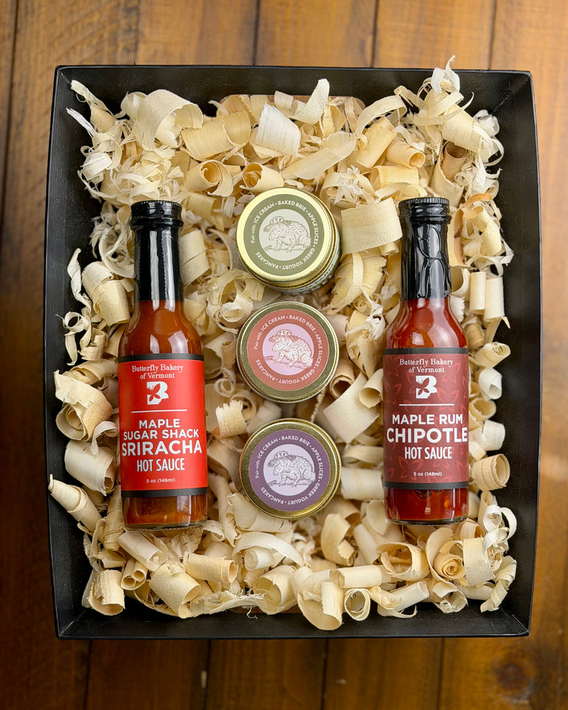 Two hot sauce bottles and three small containers of caramel in a decorative box on a wooden surface.