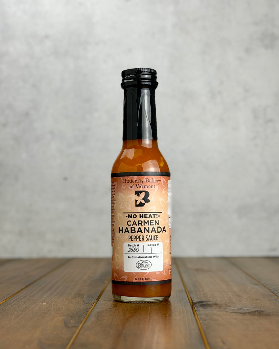 Bottle of Butterfly Bakery of Vermont's Carmen Habanada hot sauce on a wooden surface and gray background